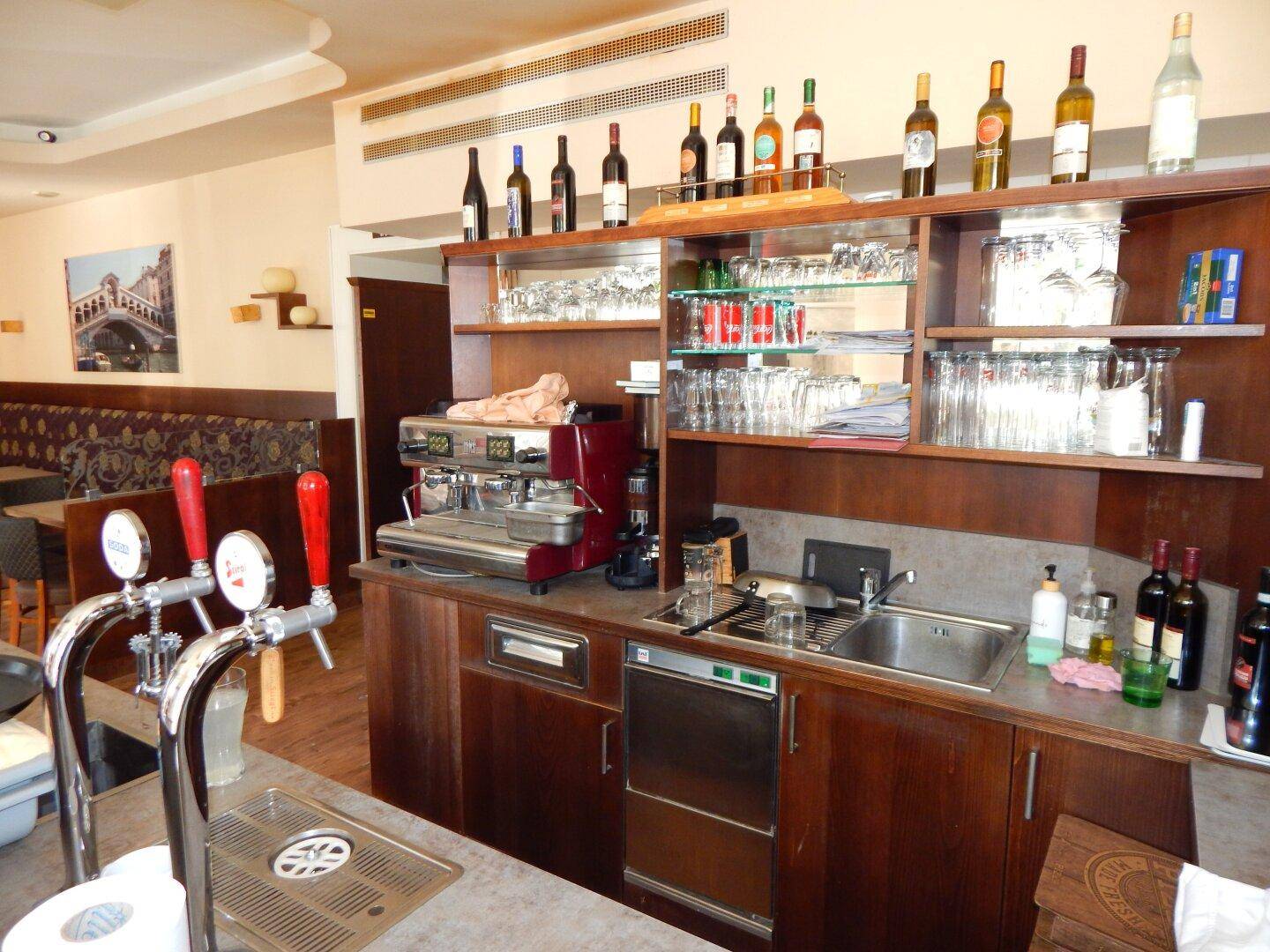 Voll ausgestatteter Barbereich mit Kaffeemaschine, Bierzapfanlage und Regalen voller Gläser und Flaschen.