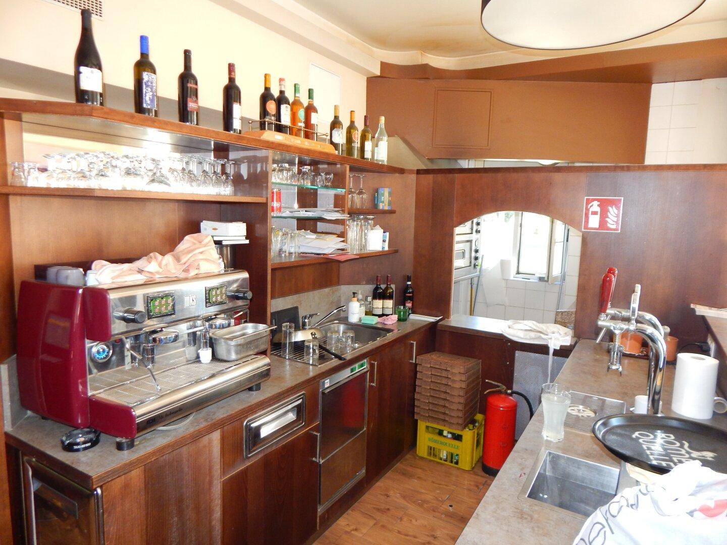 Thekenbereich einer Bar mit Kaffeemaschine, Spülbecken und einer Auswahl an Weinflaschen auf Regalen.