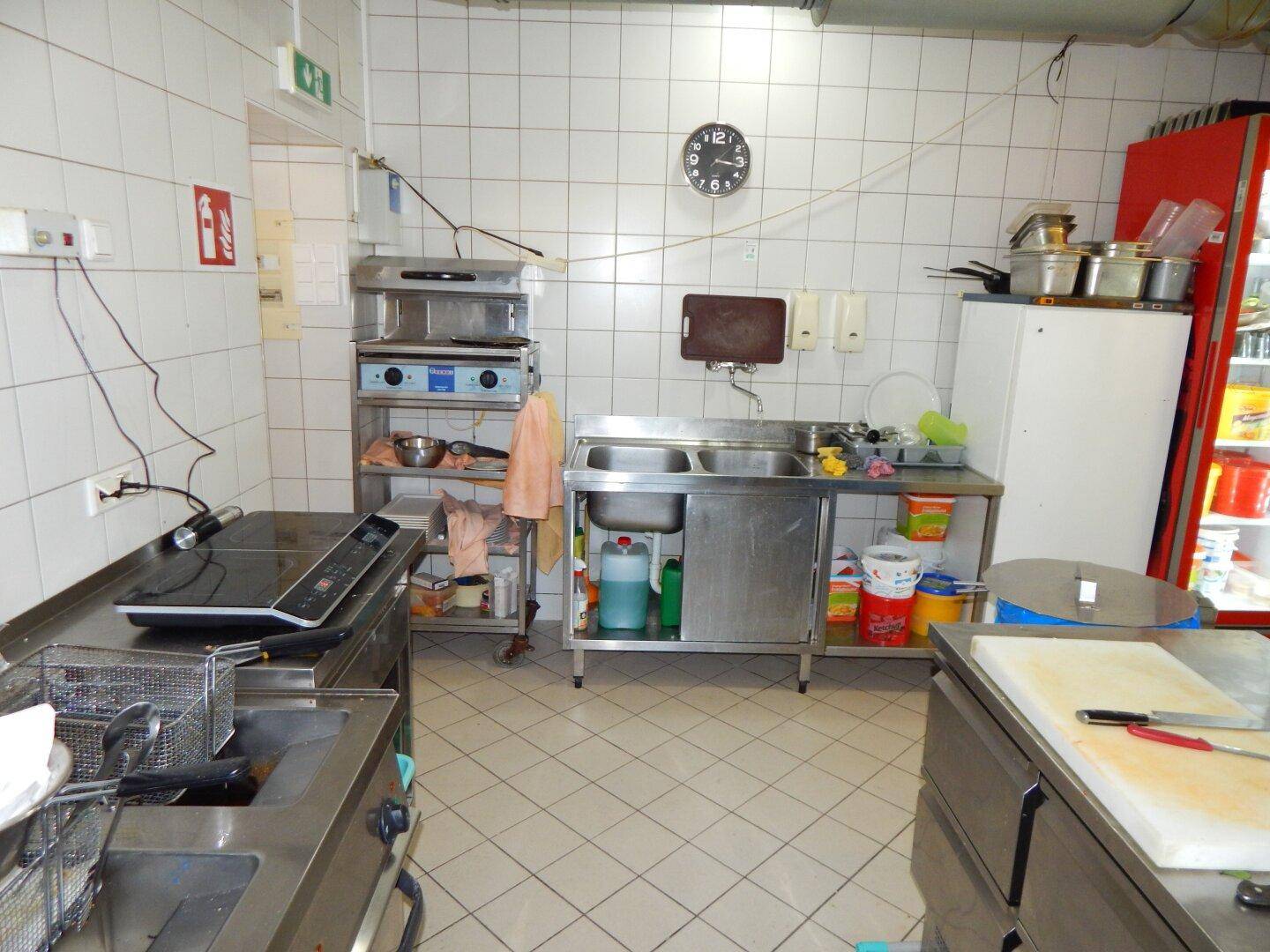 Industrielle Küche mit doppelter Edelstahlspüle, professionellen Kochgeräten und gefliesten Wänden.