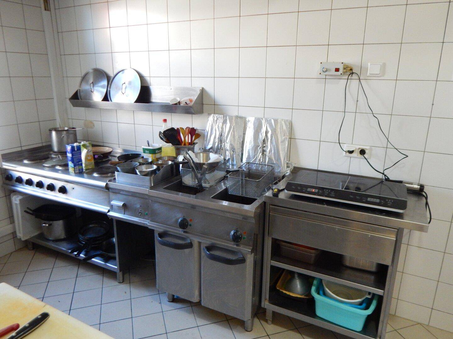 Gut ausgestattete Gewerbeküche mit mehreren Kochfeldern, Fritteusen und einer Induktionskochplatte.