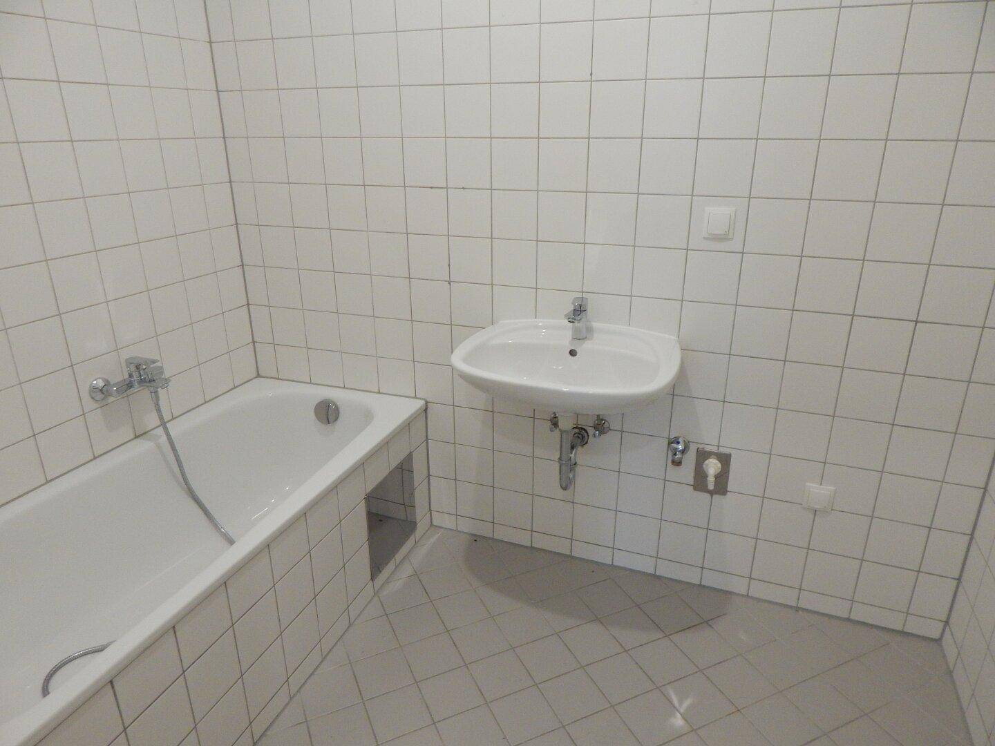 Gefliestes Badezimmer mit Badewanne und Waschbecken, in einem funktionalen Zustand.