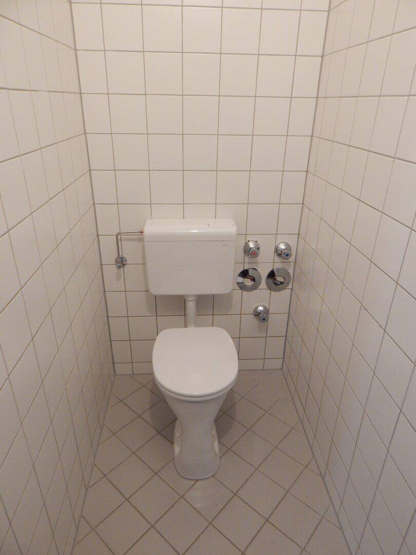 Separate Toilette mit weißen Fliesen und Standard-WC-Installation.