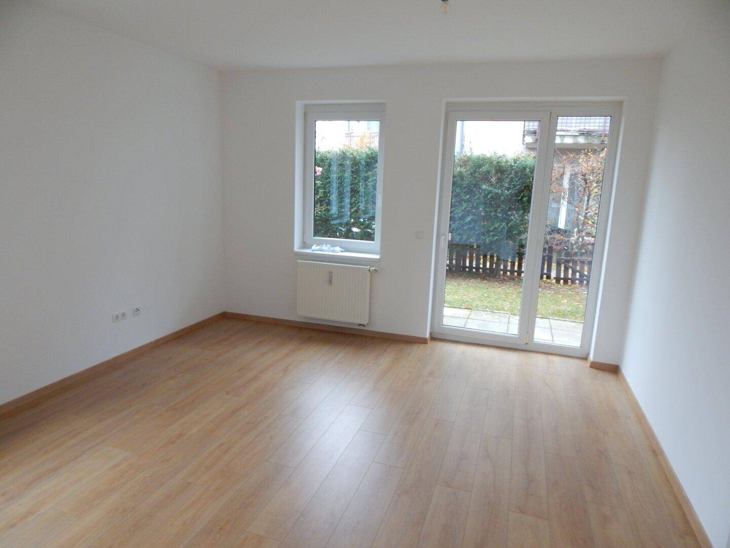 Heller Raum mit Laminatboden und großen Fenstern, die viel Tageslicht hereinlassen.