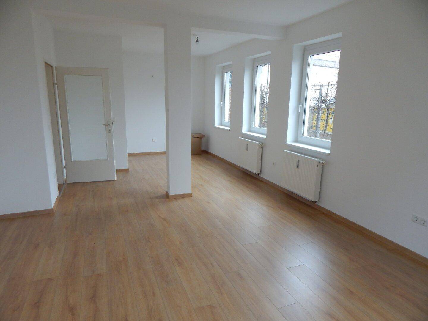 Geräumiger, heller Wohnbereich mit Laminatboden und mehreren Fenstern für viel Tageslicht.