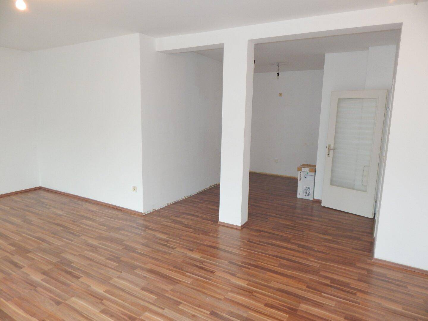 Geräumiger Innenraum mit Laminatboden und offenem Durchgang zu einem weiteren Bereich, ideal für flexible Nutzung.