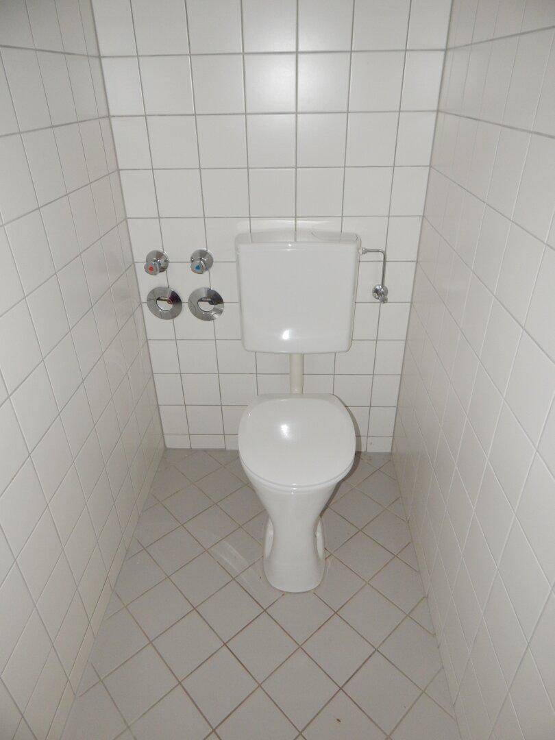 Separate Toilette mit weißen Fliesen an Wänden und Boden, sauber und funktional.