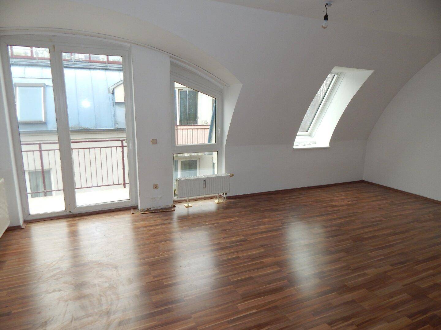 Geräumiger Wohnbereich mit Laminatboden, Dachschrägen und direktem Balkonzugang, der viel Licht hereinlässt.