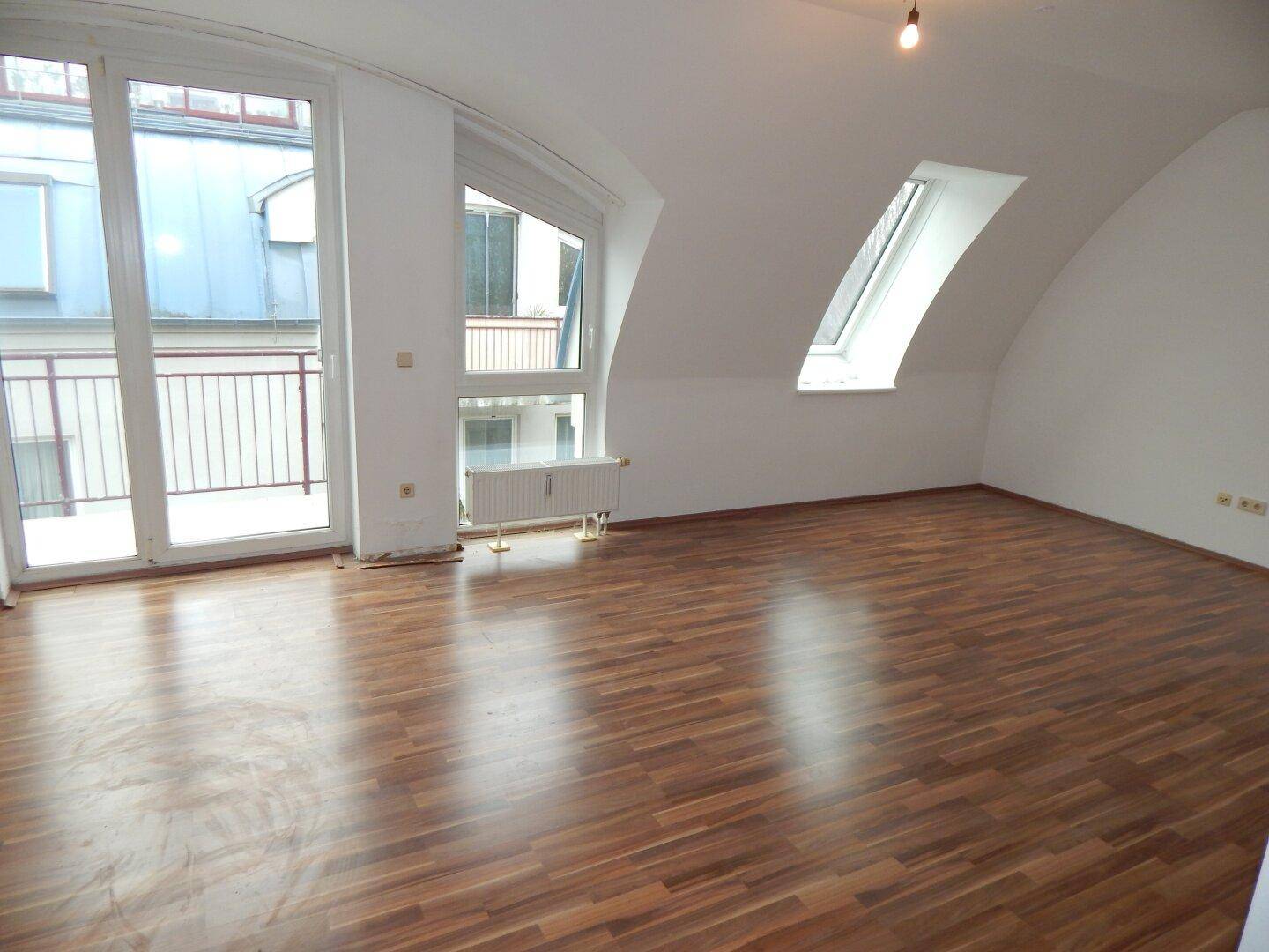 Heller Wohnraum mit Laminatboden, Dachschrägen und direktem Zugang zu einem Balkon.