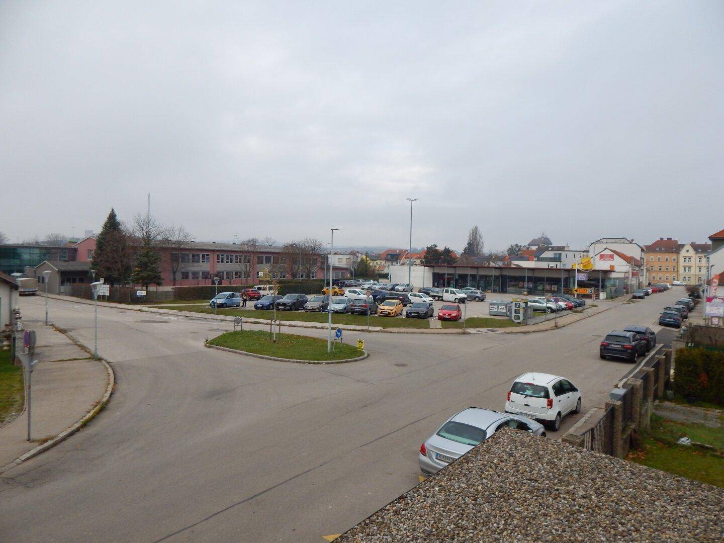 Weitläufiger Blick auf die Umgebung mit Parkplätzen, Gebäuden und einer Straße.