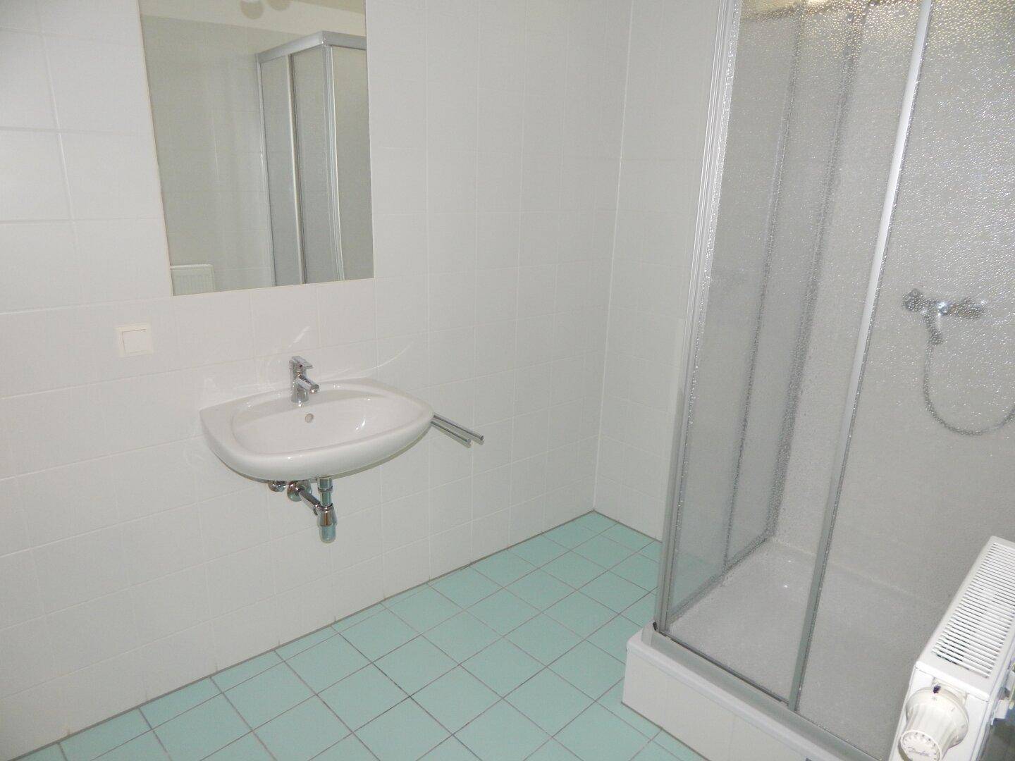 Badezimmer mit Duschkabine, Waschbecken und hellblauen Fliesen, in gutem Zustand.