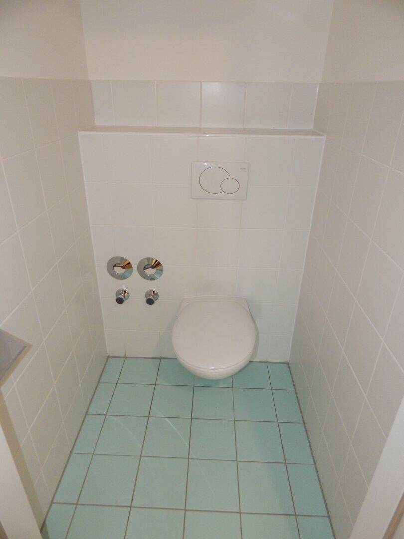 Separate Toilette mit Wand-WC und hellblauen Fliesen, sauber und funktional.