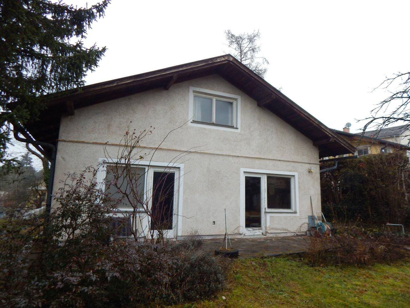 Rückseite eines Hauses mit kleiner Terrasse und Zugang zum Garten, umgeben von Sträuchern.