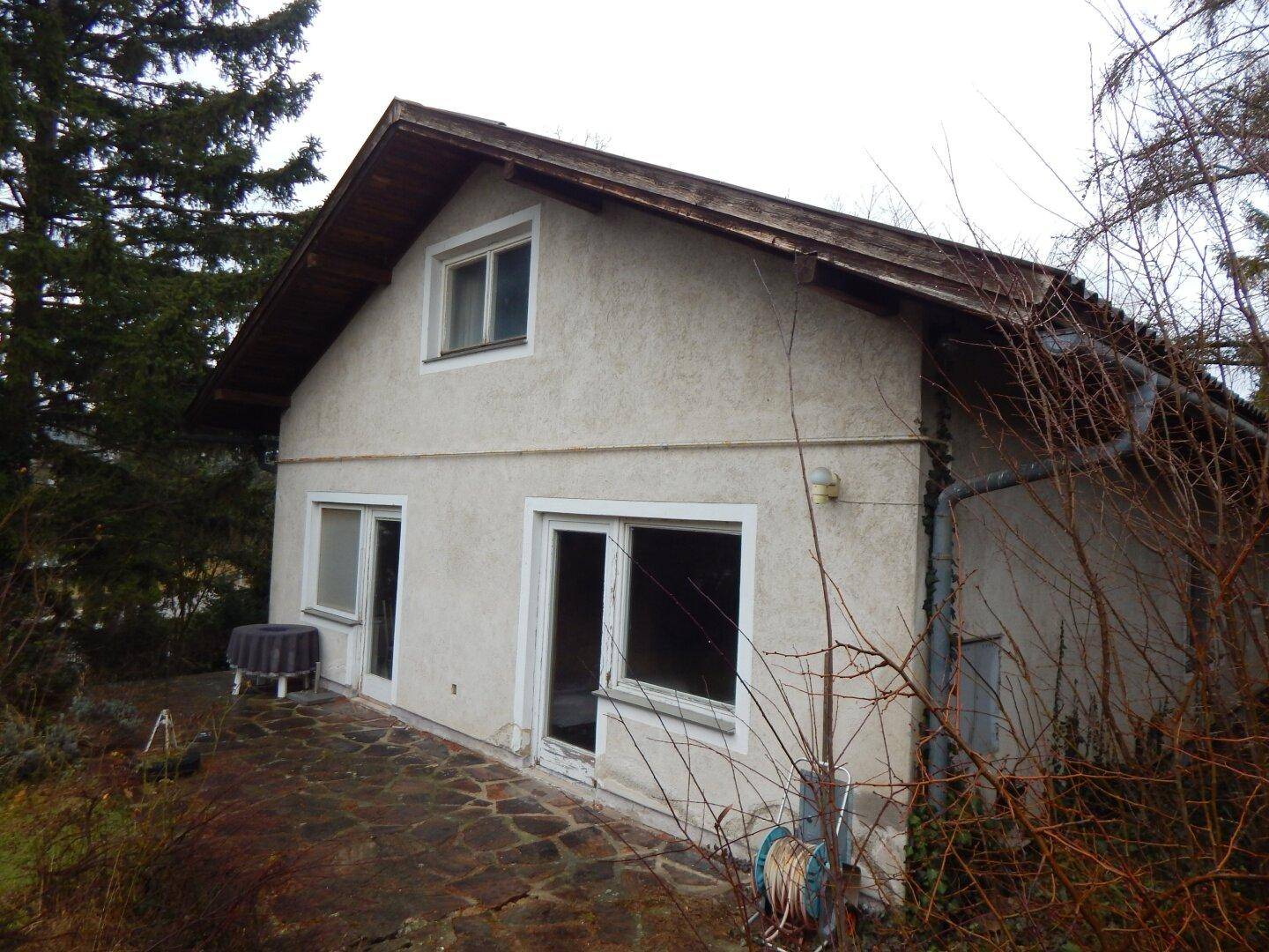 Seitliche Ansicht des Hauses mit gepflasterter Terrasse und Zugang zum Garten.
