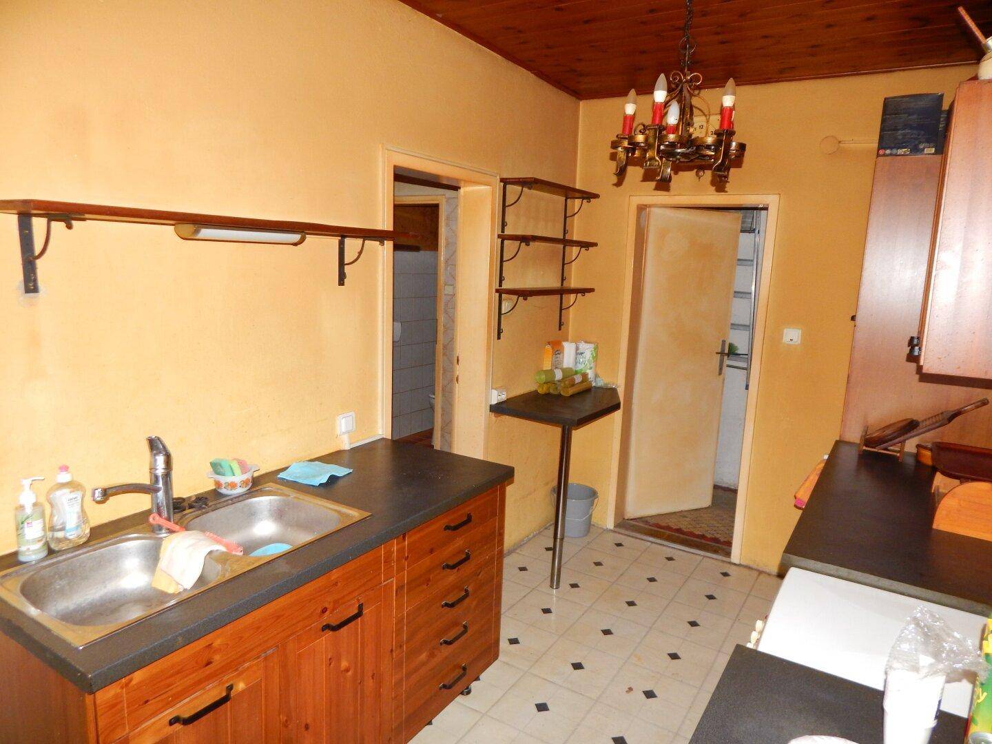 Funktionale Küche mit Holzschränken, Doppelspüle und Fliesenboden, mit Renovierungsbedarf.