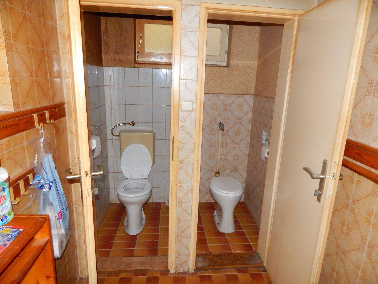 Zwei separate Toilettenräume mit Fliesenboden und Wandfliesen, in einfachem Zustand.