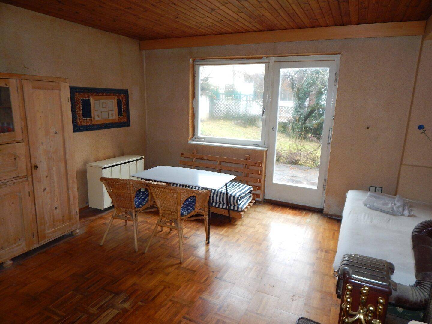 Helles Schlafzimmer mit Parkettboden, Fenster und Zugang zum Garten, mit Kaminofen.