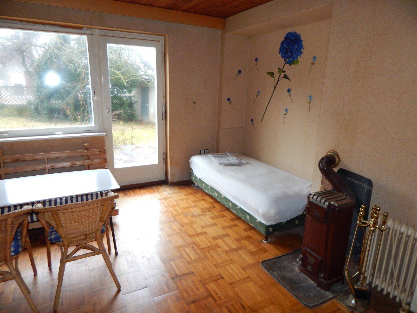 Gemütliches Schlafzimmer mit Parkettboden, Einzelbett und Kaminofen, bietet direkten Gartenzugang.