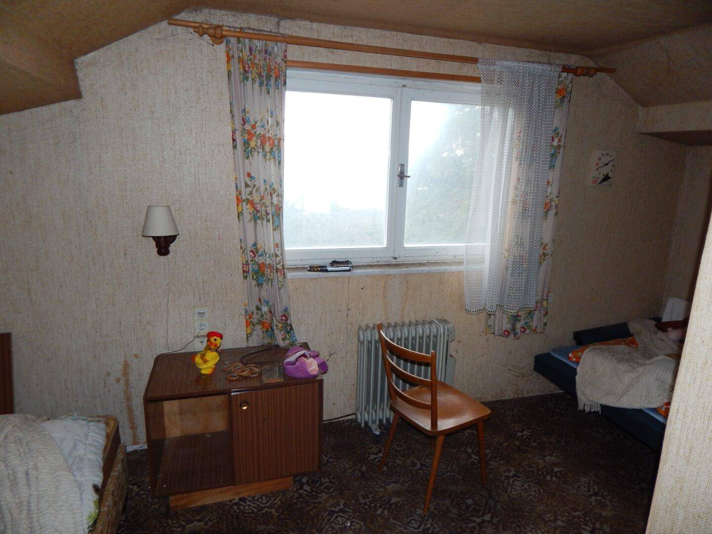 Schlafzimmer im Dachgeschoss mit Fenster und Heizkörper, in einfachem Zustand.