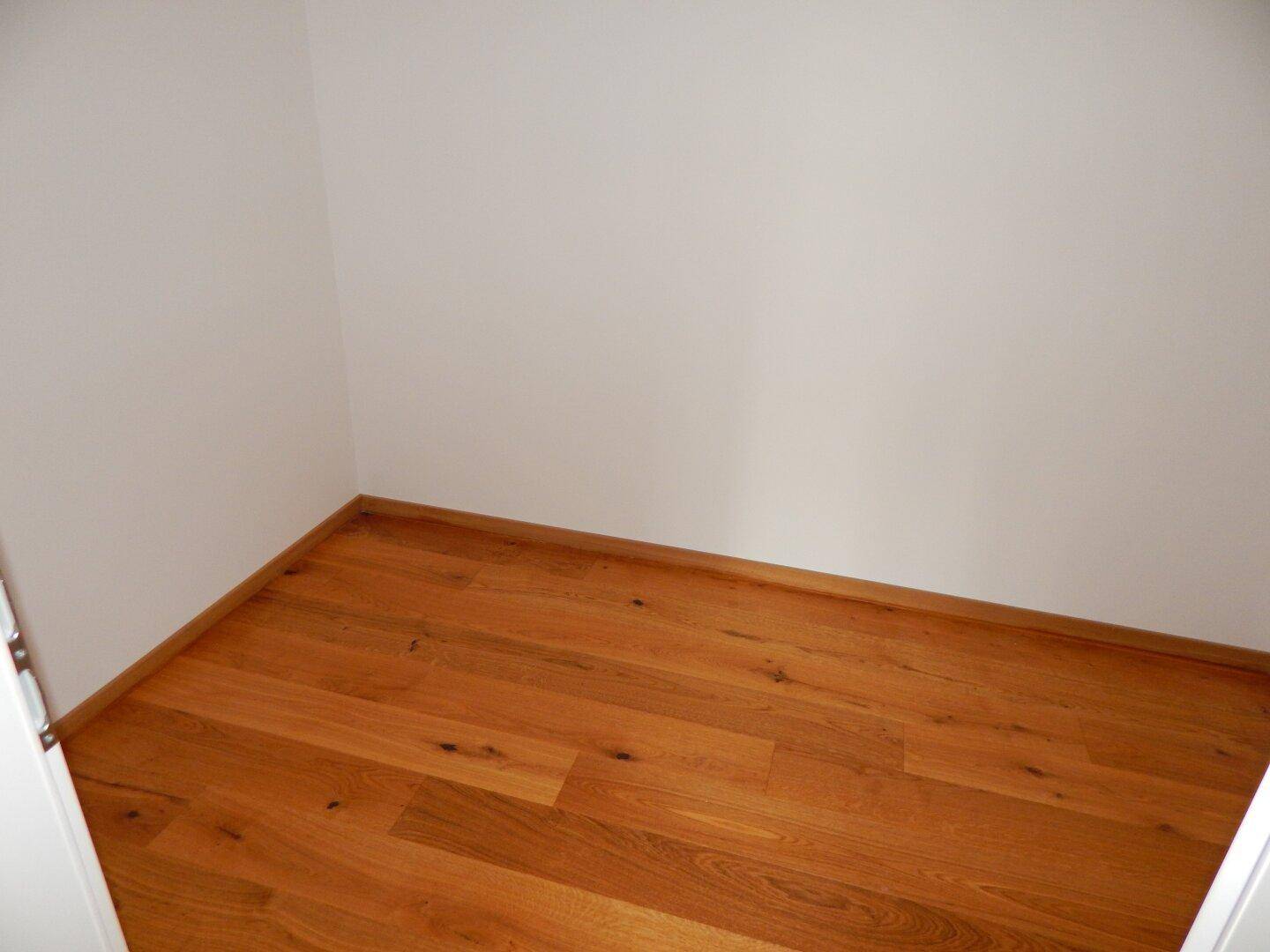 Kleiner, leerer Raum mit Holzboden, ideal als Abstellraum oder begehbarer Kleiderschrank nutzbar.