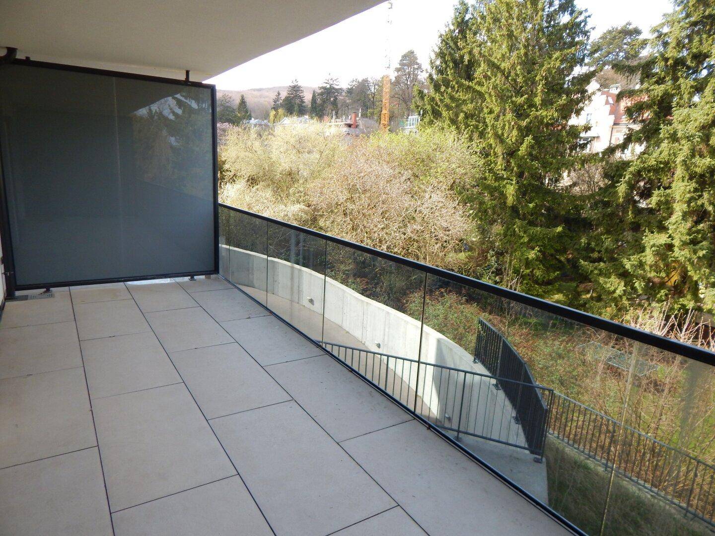 Heller Balkon mit Fliesenboden und schöner Aussicht auf die bewaldete Umgebung und den Horizont.