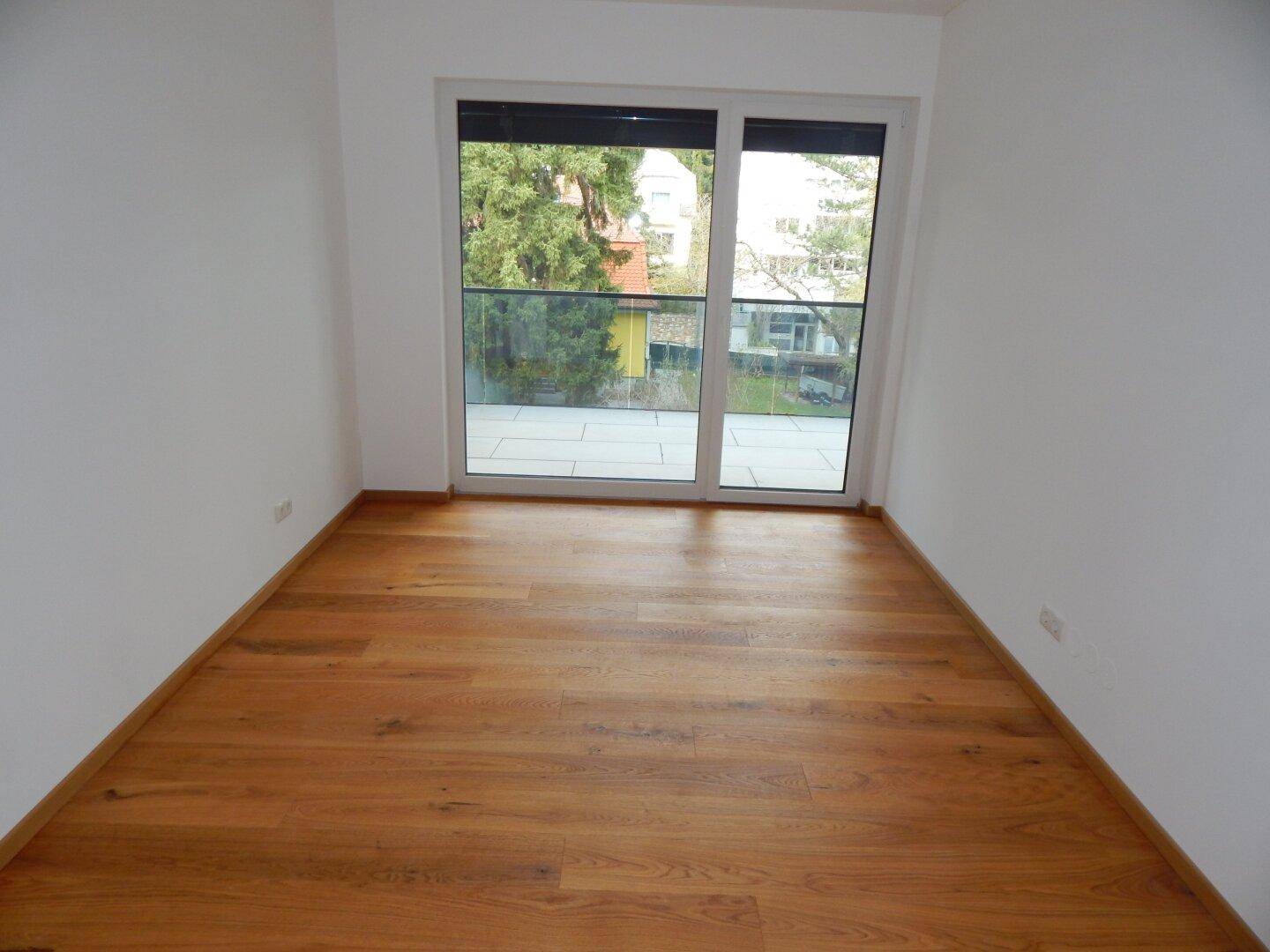 Helles Schlafzimmer mit Holzboden und großem Fenster, das direkten Zugang zum Balkon bietet.