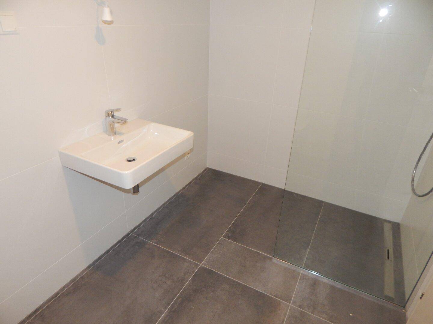 Modernes Badezimmer mit ebenerdiger Dusche, Wandwaschbecken und großformatigen grauen Fliesen.