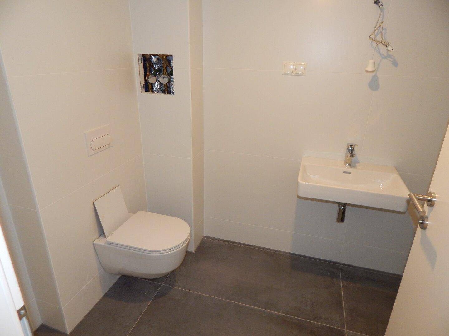 Helles Gäste-WC mit wandhängender Toilette, modernem Waschbecken und grauen Bodenfliesen.