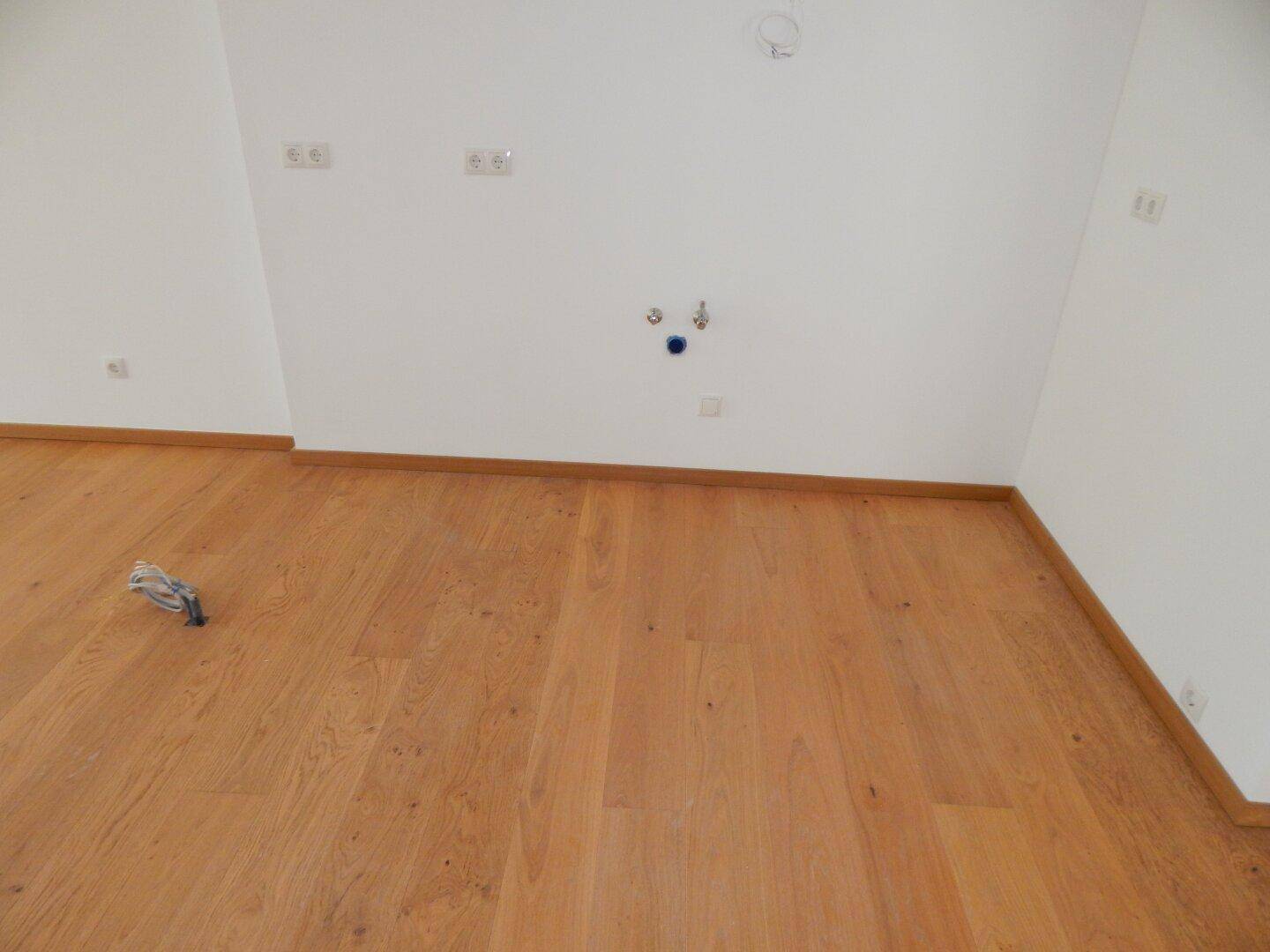 Leerer Küchenbereich mit allen notwendigen Anschlüssen für eine zukünftige Einbauküche und Holzboden.