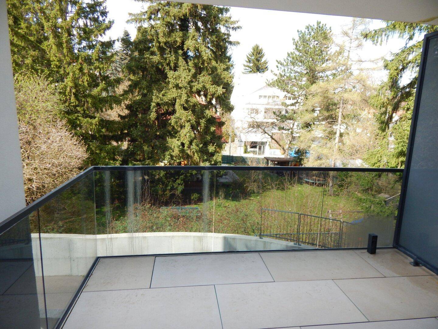 Moderner Balkon mit Glasgeländer und weitem Blick auf Bäume und die umliegende Natur.