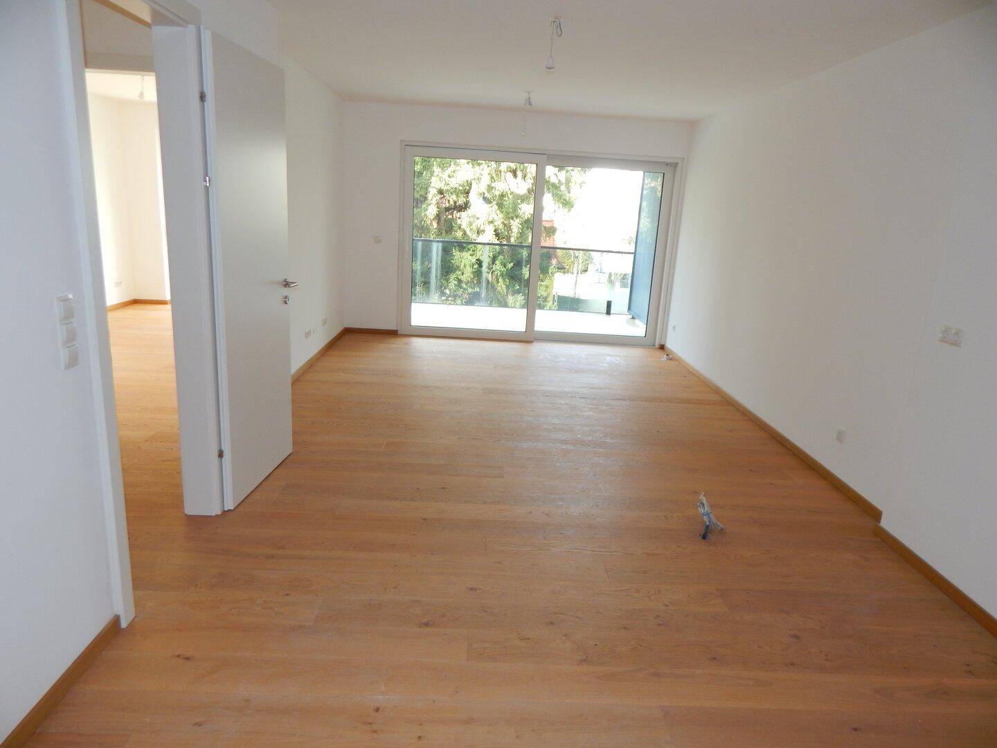 Geräumiges Wohnzimmer mit Holzboden und breiter Schiebetür, die zu einem Außenbereich führt.