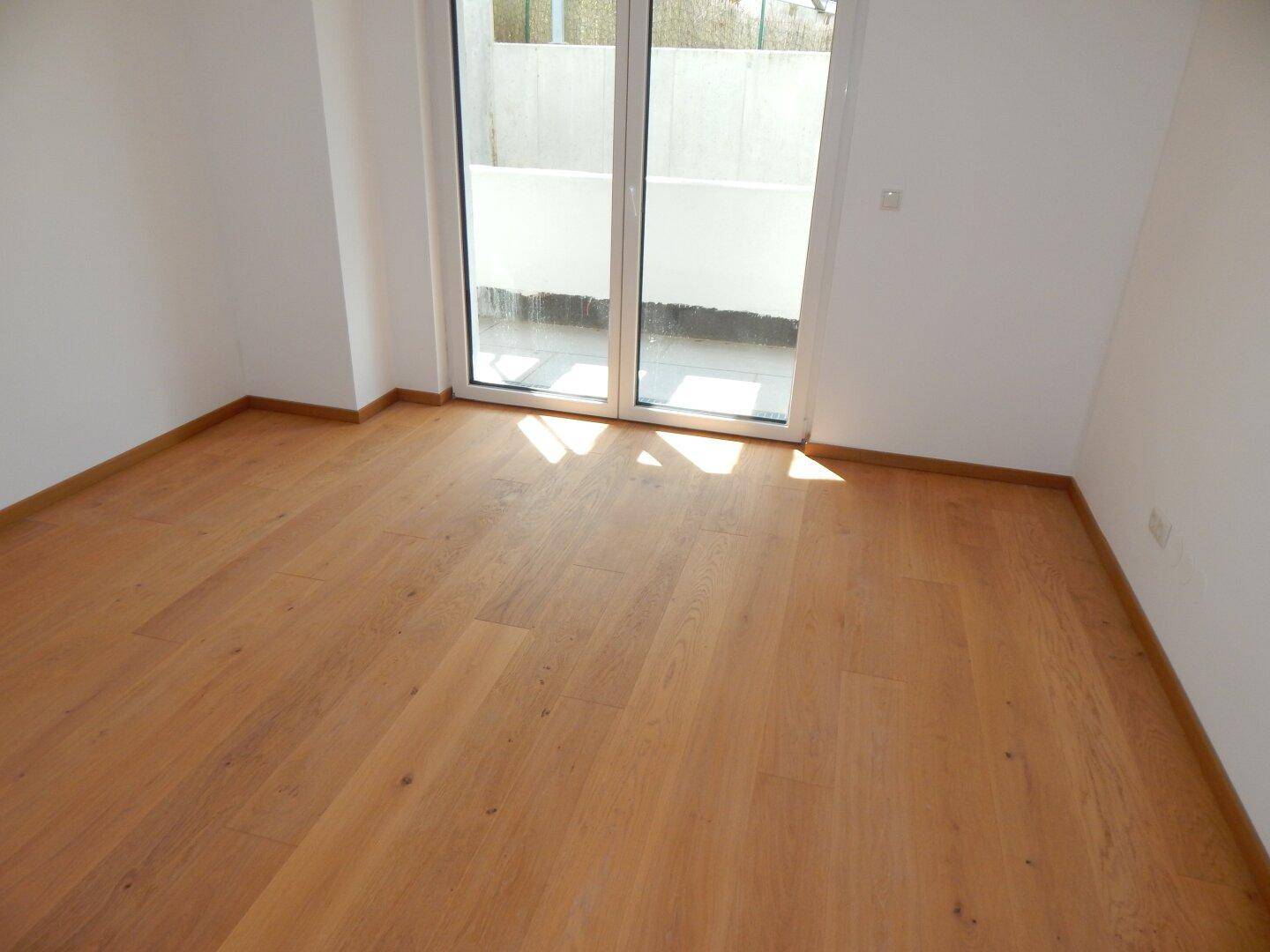 Schlafzimmer mit Holzboden und direktem Zugang zu einem sonnigen Außenbereich.