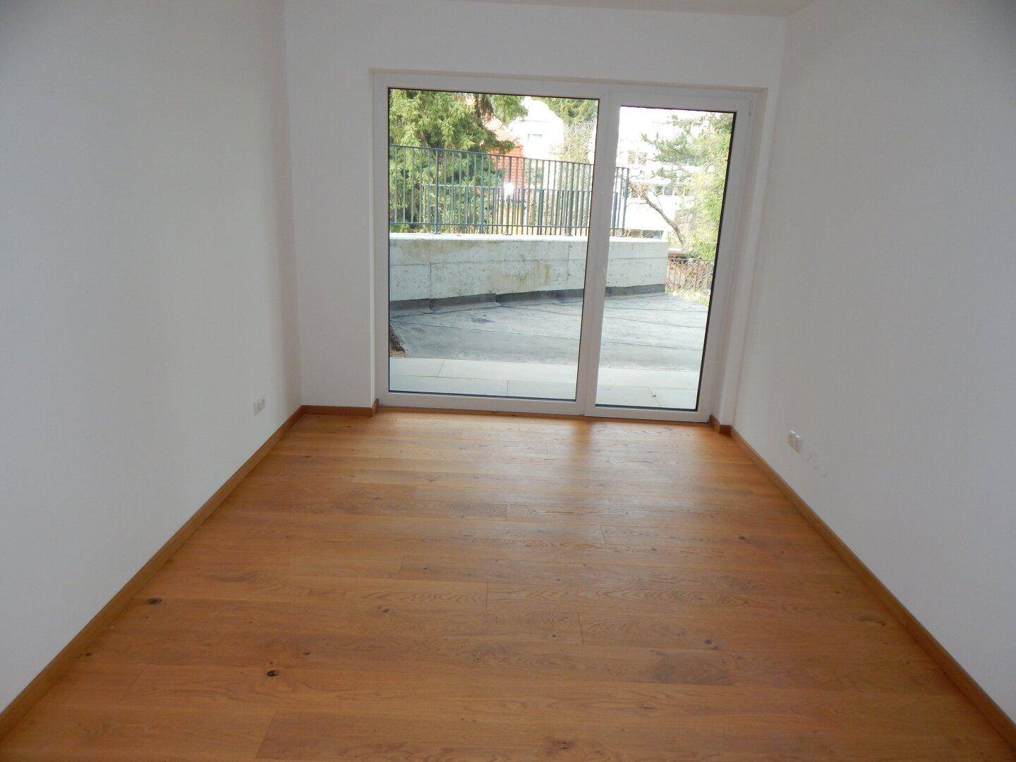 Helles Schlafzimmer mit Holzboden und großer Glasschiebetür zum Außenbereich.