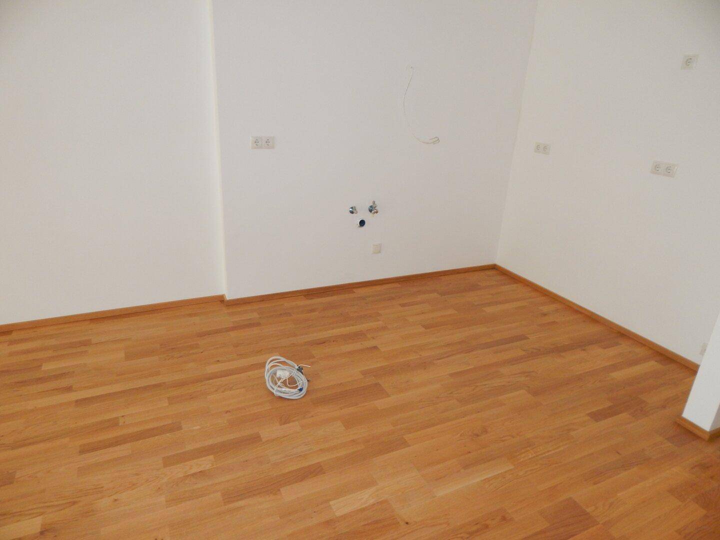 Leerer Raum mit Parkettboden und Wandanschlüssen, bereit für individuelle Gestaltung.