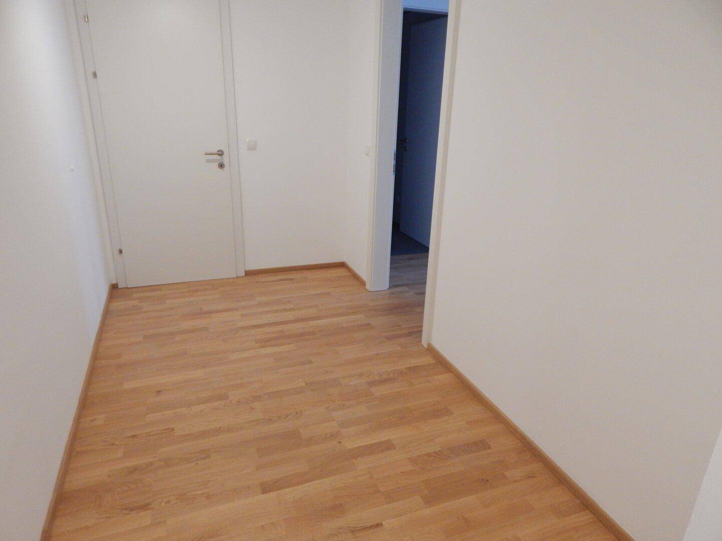 Heller Flur mit Parkettboden und weißen Türen, der zu weiteren Räumen führt.