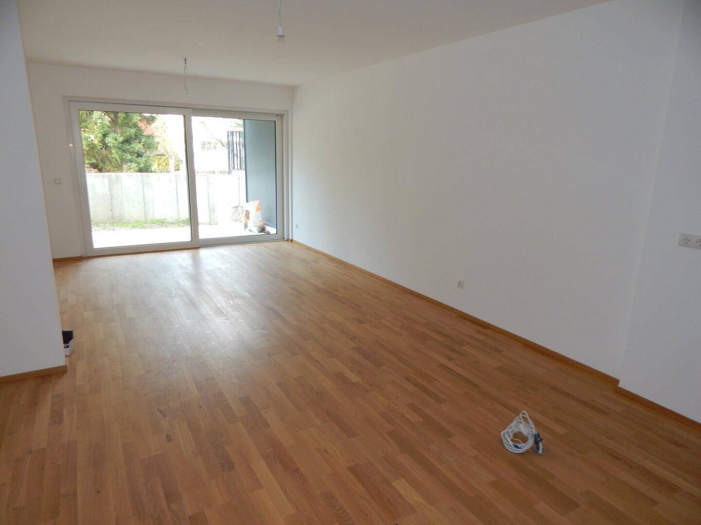 Geräumiges Wohnzimmer mit hellem Parkettboden und direktem Zugang zum Außenbereich.