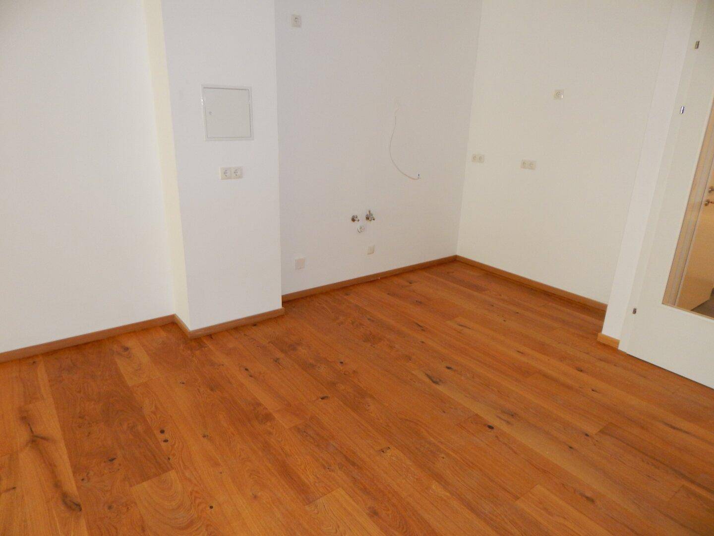 Leerer Raum mit Holzboden und weißen Wänden, bereit für die individuelle Gestaltung.
