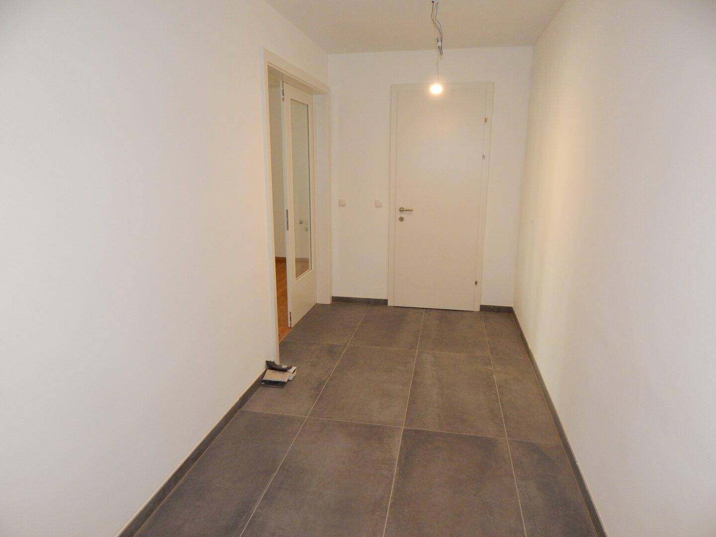 Heller Flur mit grauen Bodenfliesen und weißen Wänden, der zu weiteren Räumen führt.