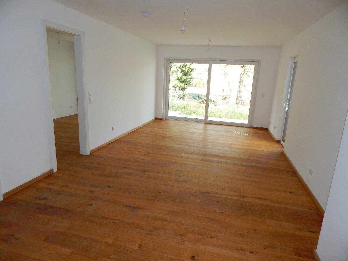 Helles, leeres Wohnzimmer mit Holzboden und großer Schiebetür zum Garten.
