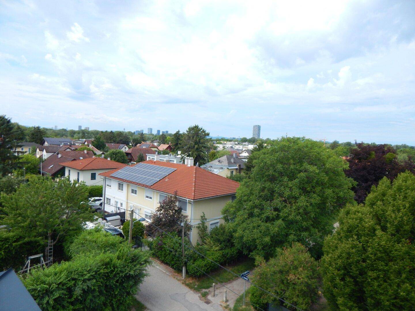 Weitläufiger Ausblick über eine grüne Wohngegend mit vielen Dächern und Bäumen in der Ferne.