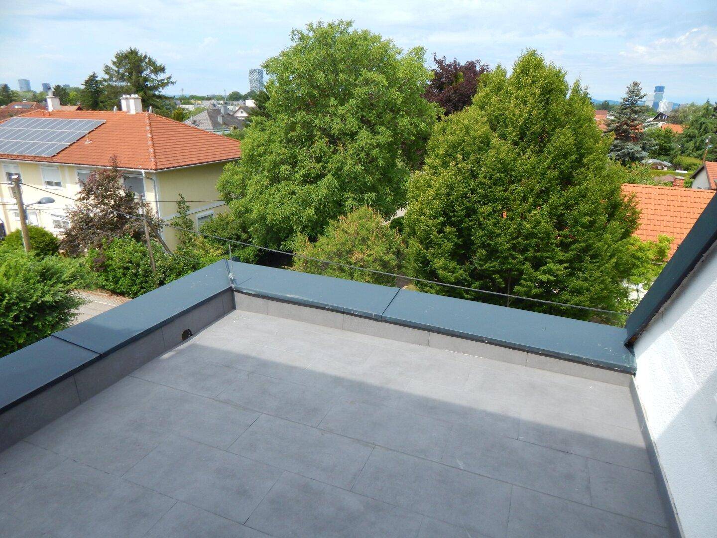 Aussicht von einem Dach über grüne Bäume und Dächer von Wohnhäusern in der Umgebung an einem sonnigen Tag.