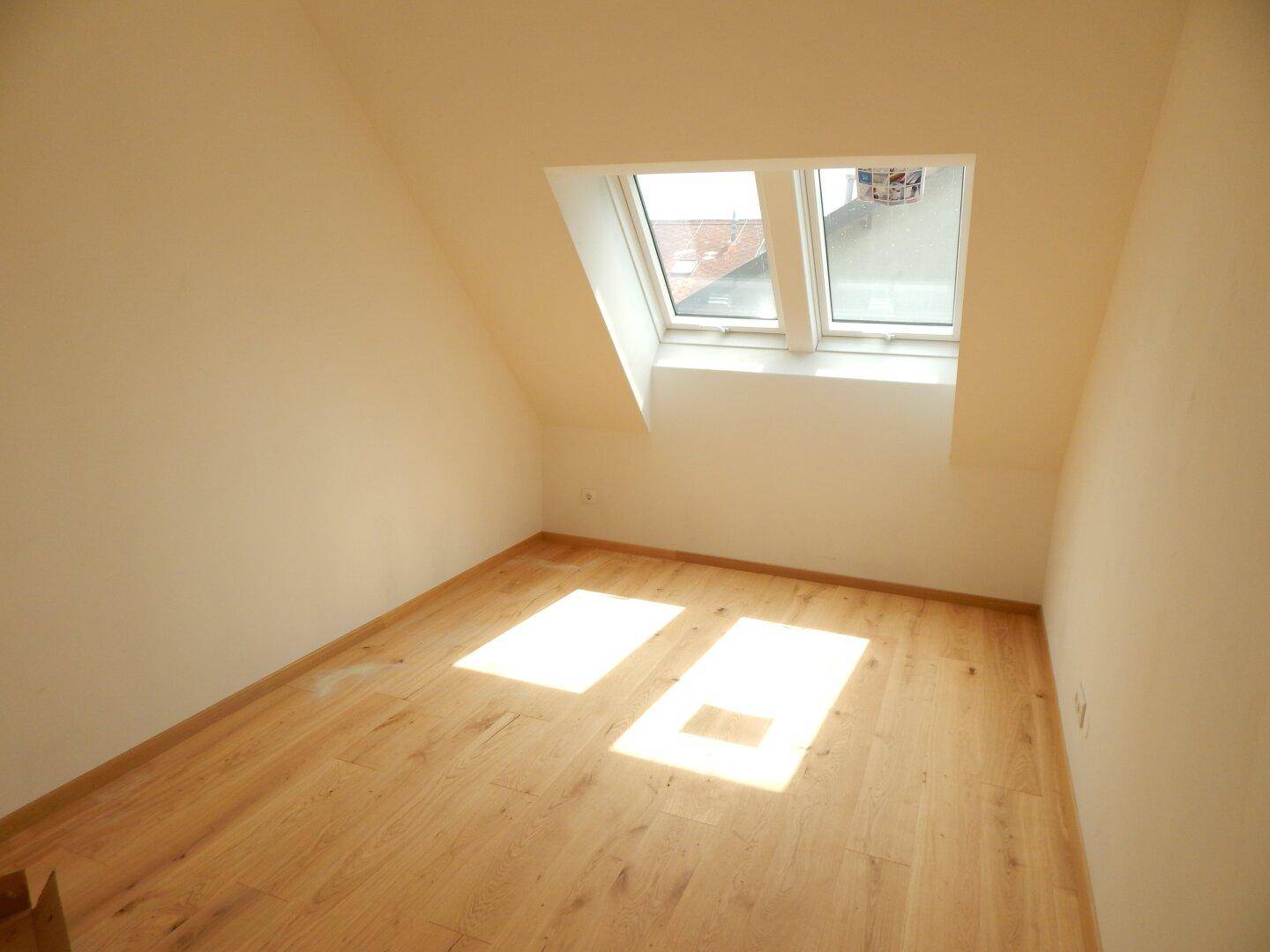 Lichtdurchfluteter Raum mit hellem Holzboden und Dachfenstern, perfekt für ein Kinderzimmer oder Gästezimmer.