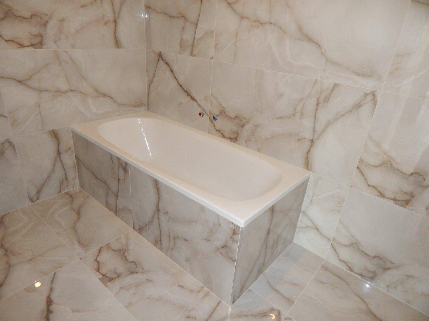 Modernes Badezimmer mit eleganten Marmorfliesen an Wänden und Boden sowie einer Badewanne.