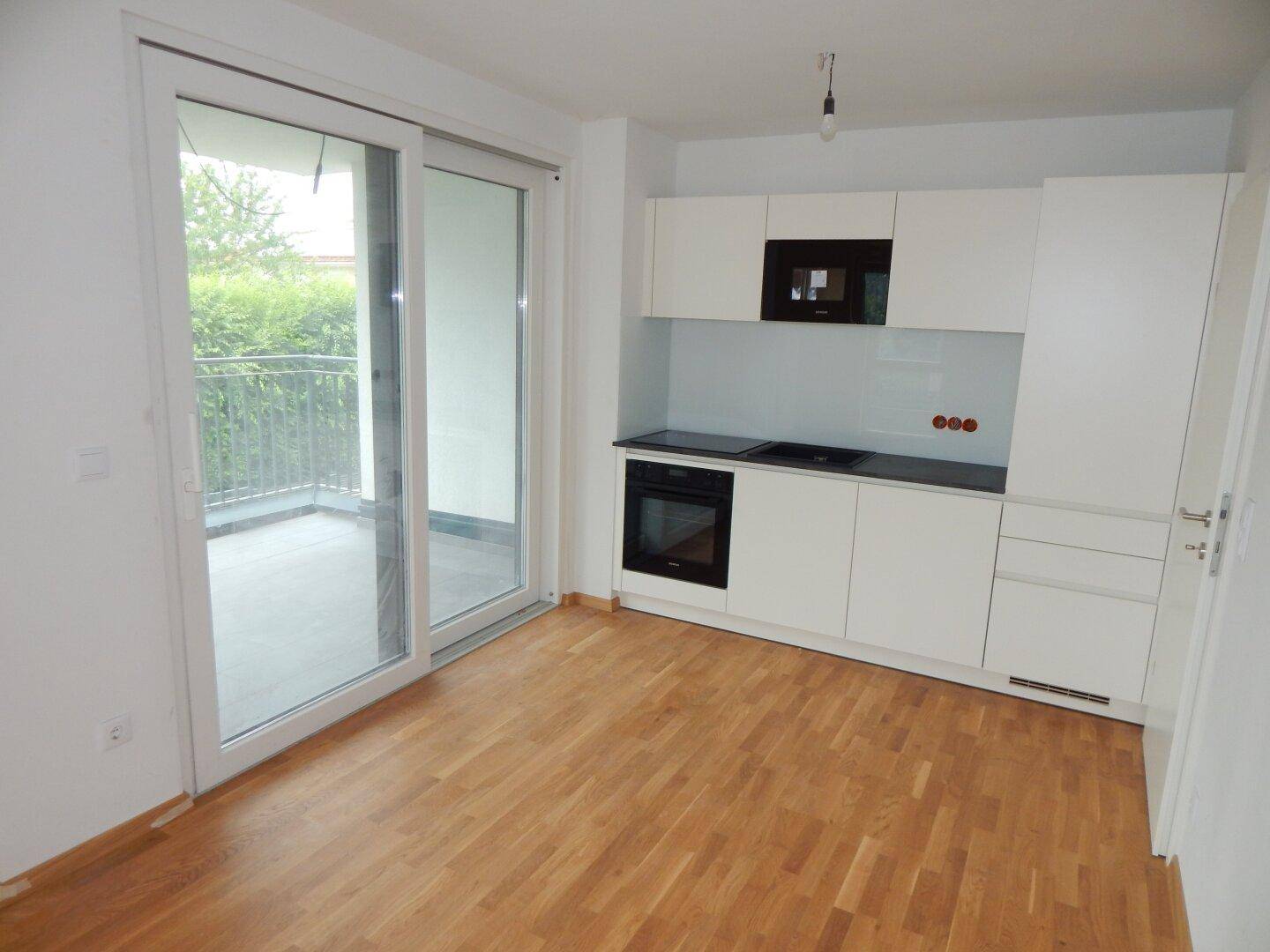 Moderne Küchenzeile mit weißen Schränken, integriertem Backofen und Zugang zu einem Balkon.