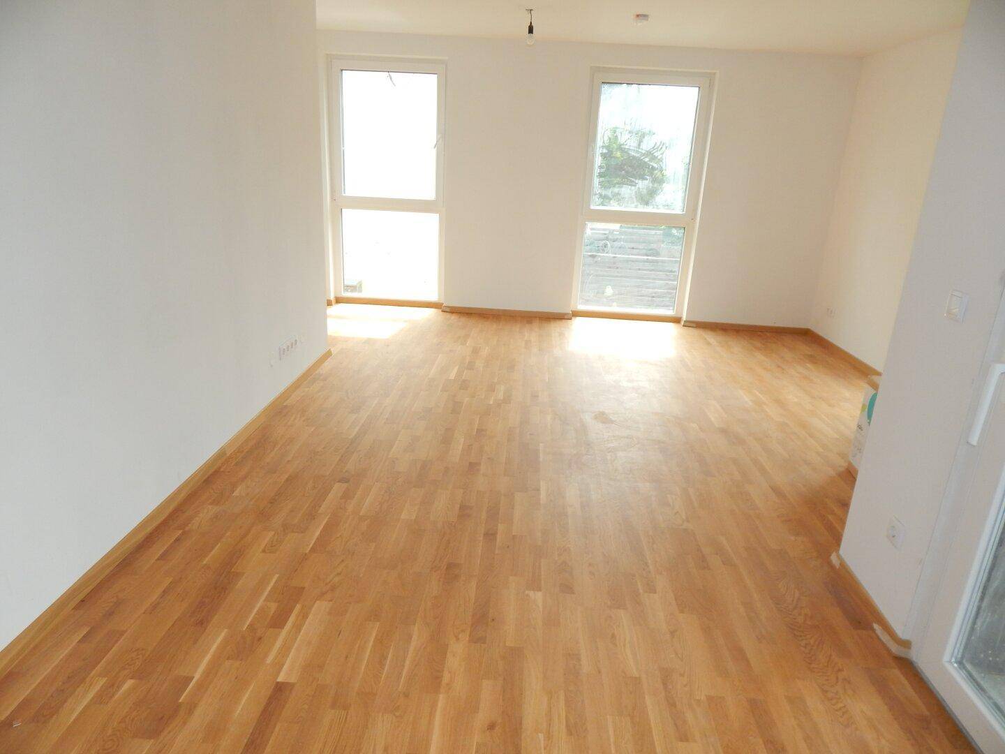 Geräumiger, heller Raum mit Holzboden und großen Fenstern, ideal für individuelle Gestaltung.