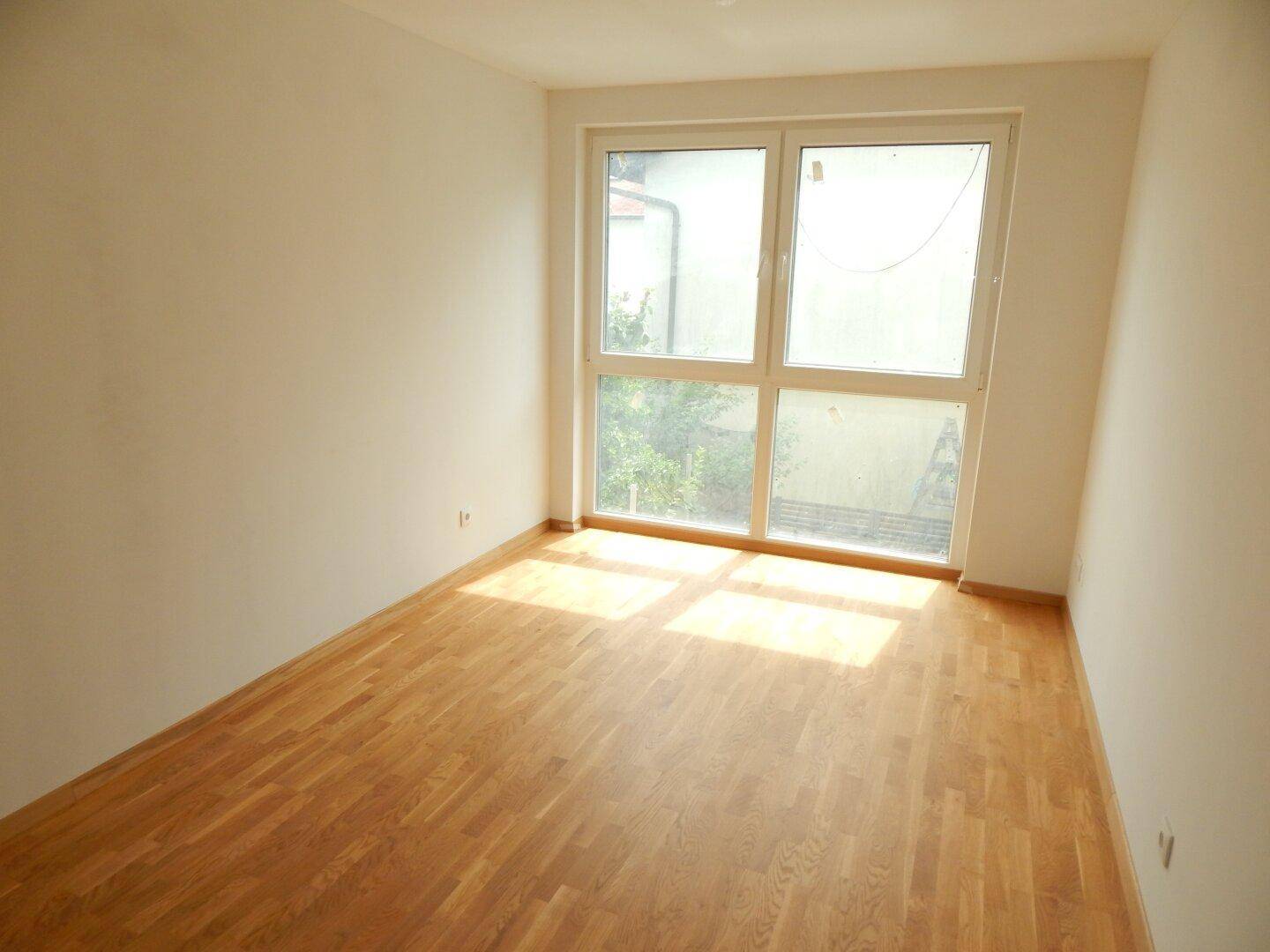 Gemütliches Zimmer mit Parkettboden und großem Fenster, das für eine helle Atmosphäre sorgt.