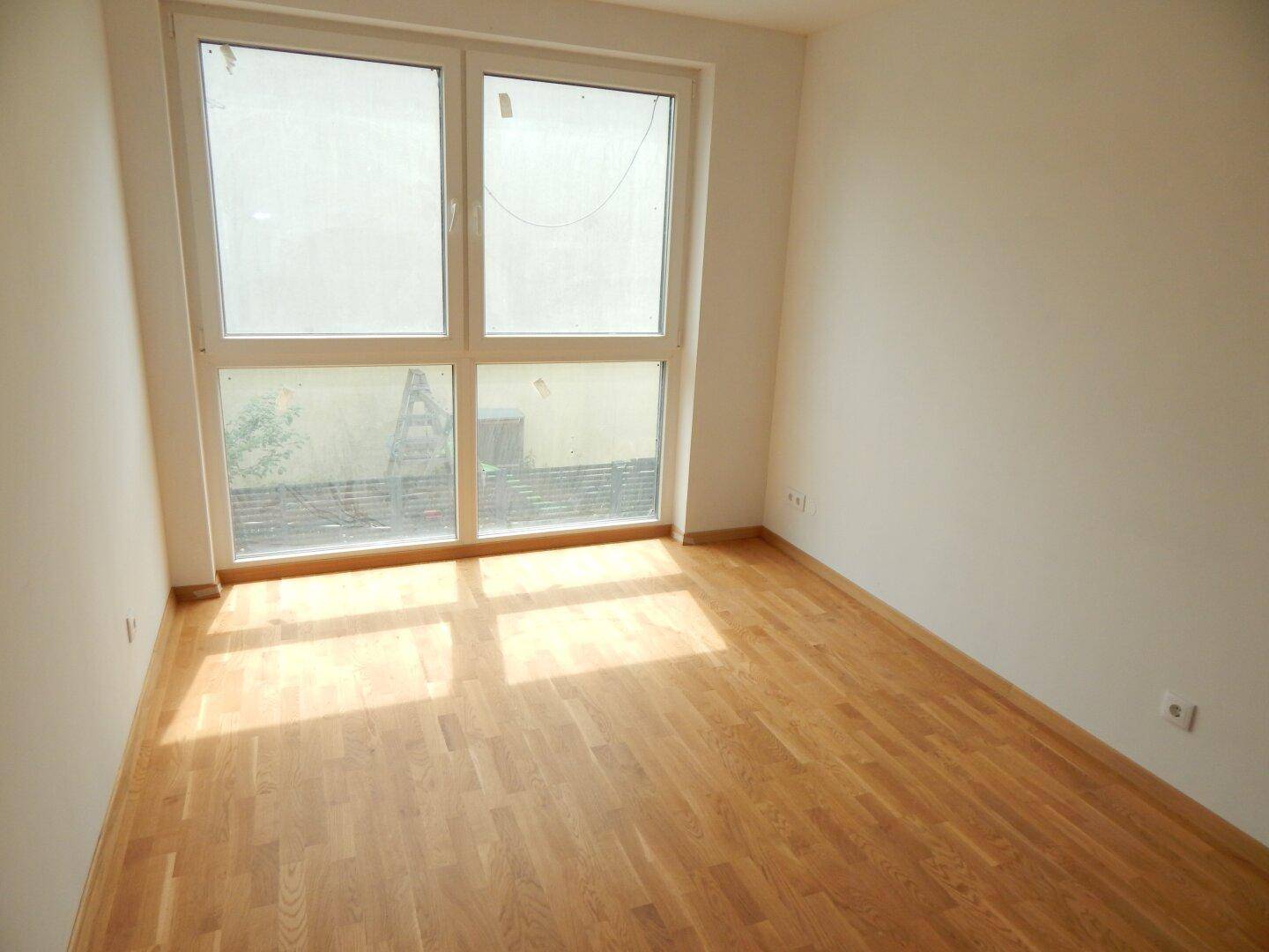 Helles Schlafzimmer mit Holzboden und einem großen Fenster, das viel Sonnenlicht einfängt.