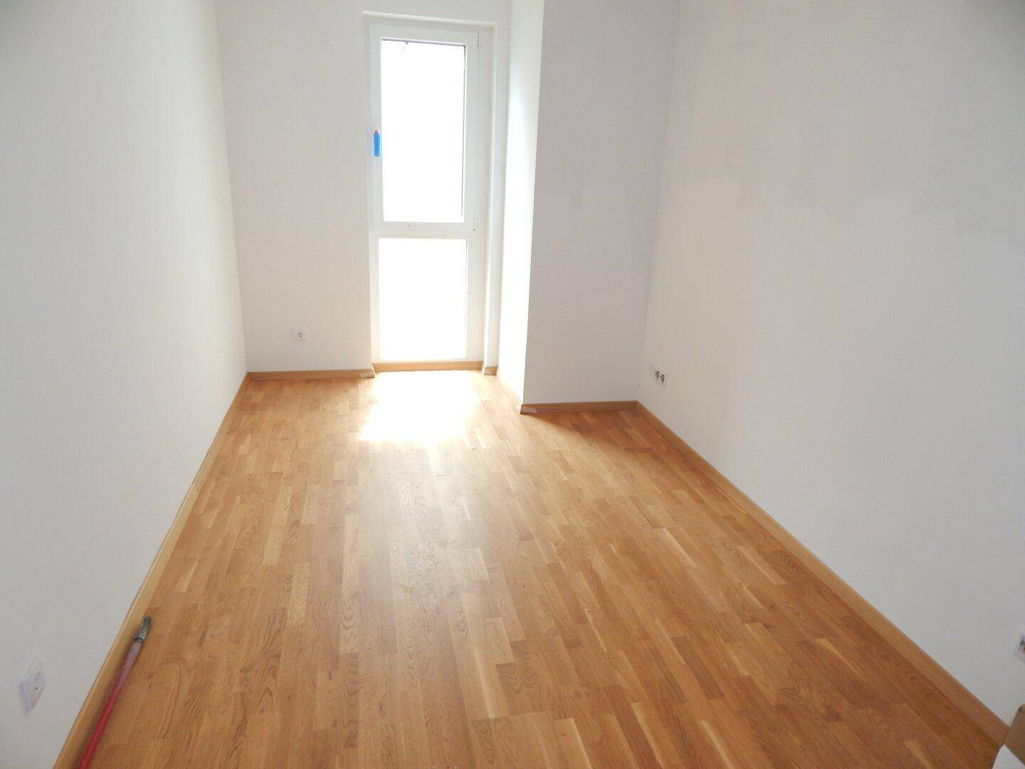 Heller Raum mit Parkettboden und einer Balkontür, die Zugang zum Außenbereich bietet.