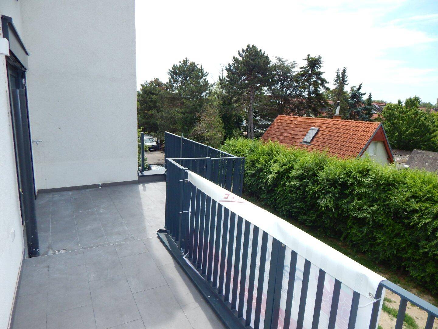 Balkon mit Metallgeländer und Blick auf die umliegenden Häuser und viel Grün.
