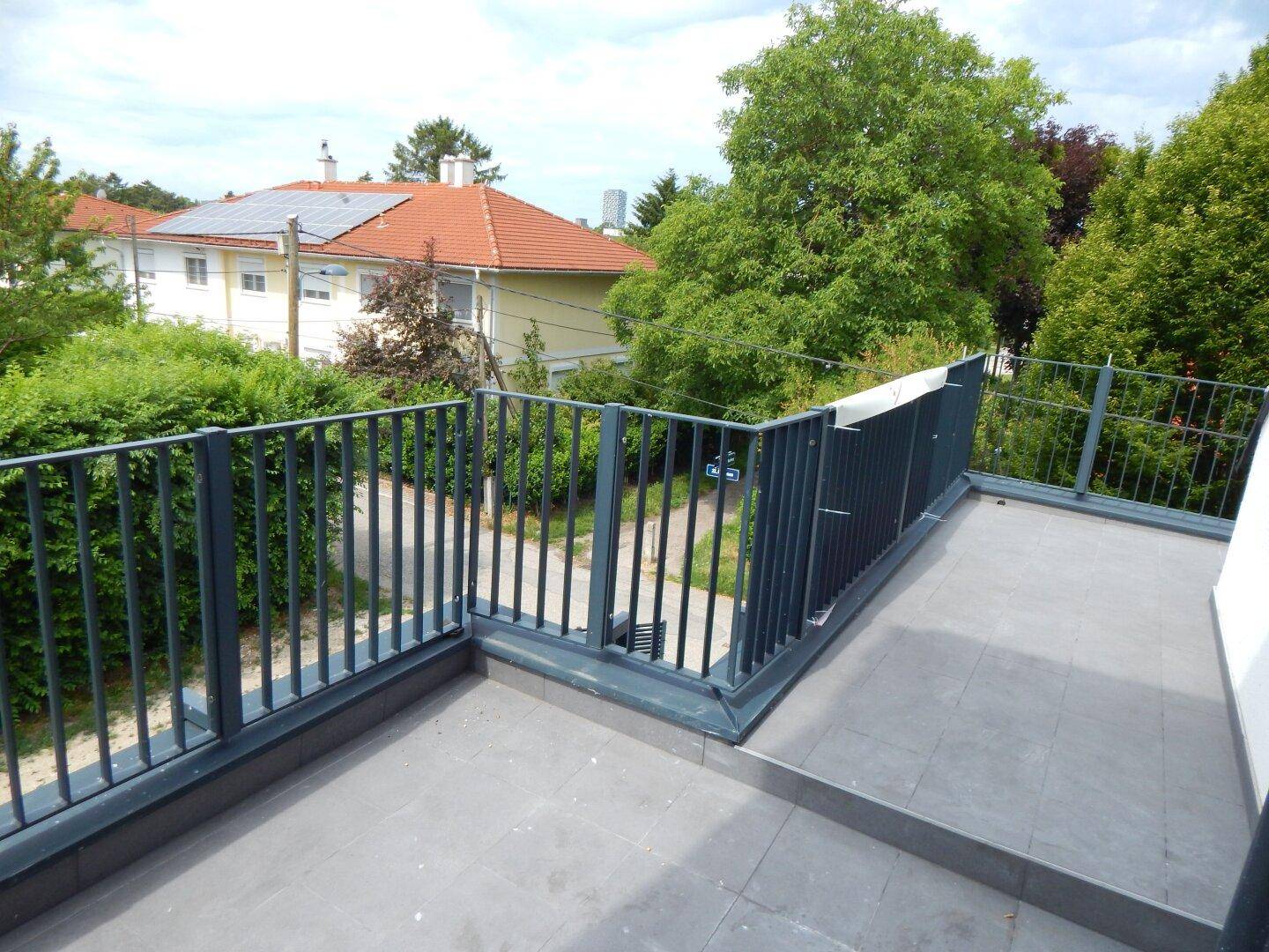 Balkon mit moderner Brüstung und weitem Blick über die grüne Umgebung und Dächer.
