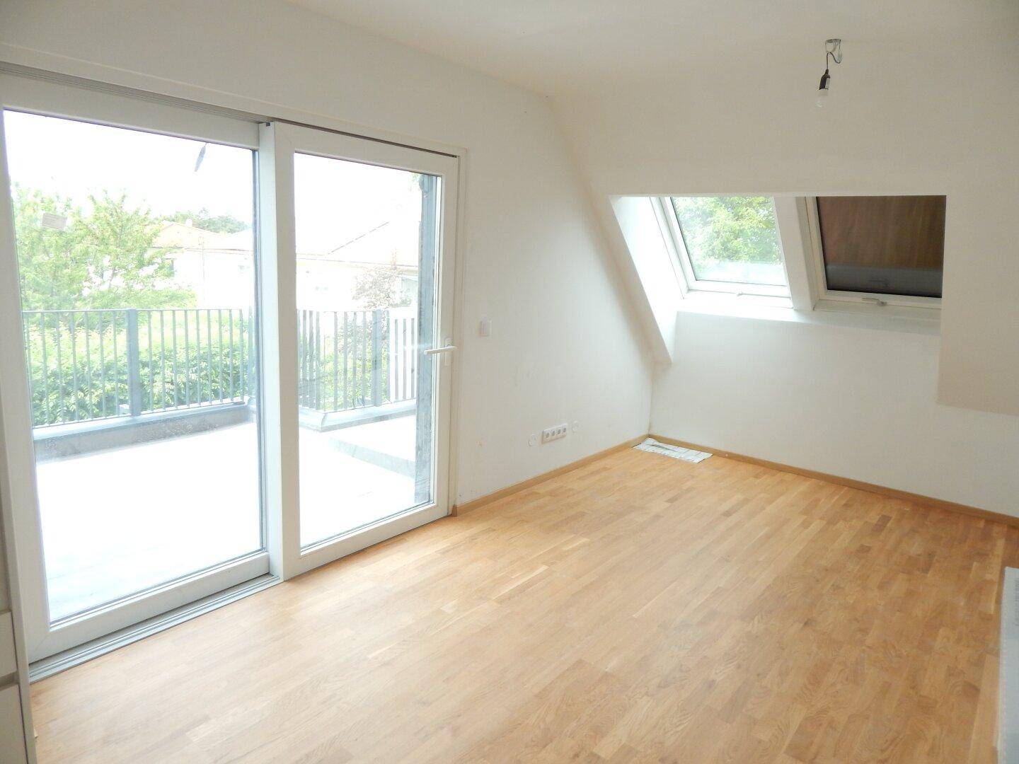 Heller Raum mit Holzboden, großen Schiebetüren zum Balkon und Dachfenster, ideal als Wohnzimmer.